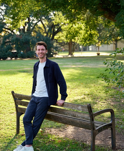 Chris Mijatovich outdoors, seated on a park bench under trees